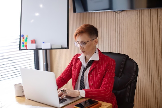 Shot of an attractive mature businesswoman in red suit working on laptop in her workstation