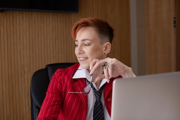 빨간색 슈트를 입은 매력적인 성숙한 사업가 여성이 작업장에서 노트북에서 작업하는 사진