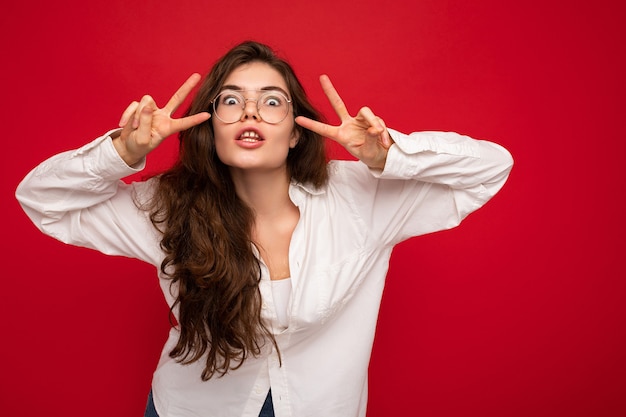 Colpo di una giovane donna castana riccia e felice, positiva, felice, divertente, che indossa una camicia bianca e