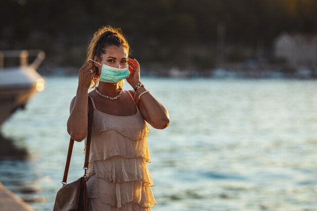Shot of an attractive young woman wearing a surgical mask while enyoing herself during walk promenade by the sea.