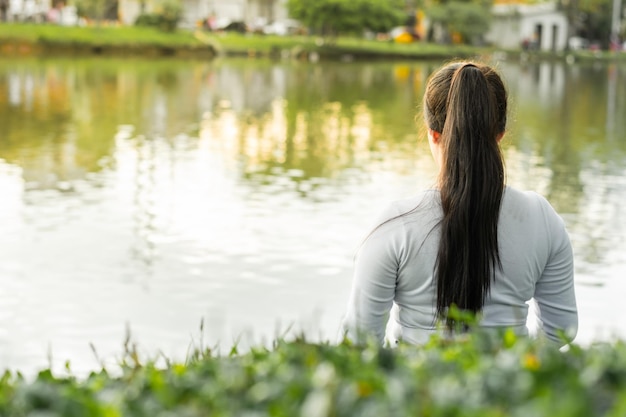 夕日を眺めながら湖のそばに座っている若い女性の背中のショット