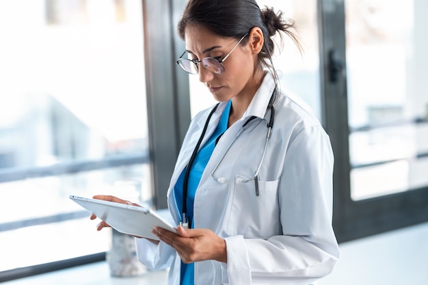 Shot of beautiful female doctor using her digital tablet while standing in the consultation.