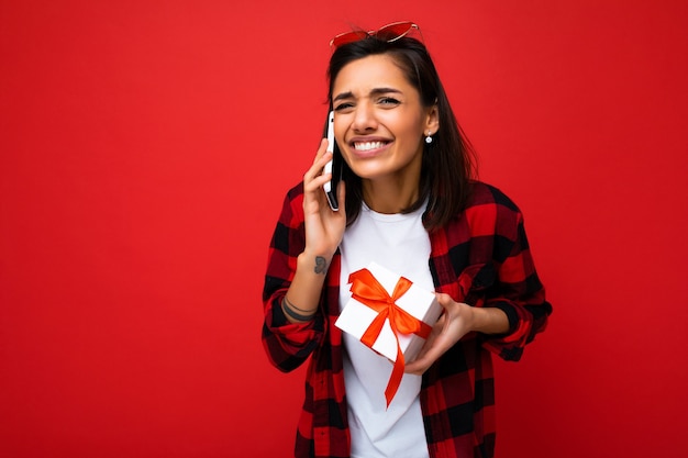 Shot of beautiful happy emotional young brunette woman isolated over red background wall wearing