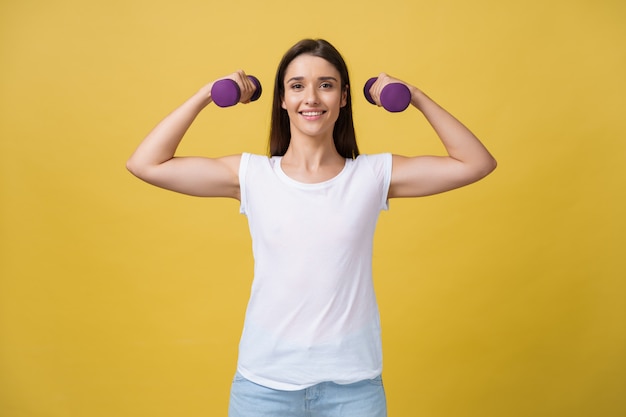 黄色の背景に対して体重を持ち上げている、美しくスポーティな若い女性のショット。