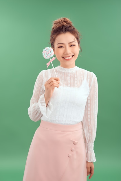 Shot of beautiful young Asian woman. Pretty girl holding round candy and cheerfully smiling. Isolated green background