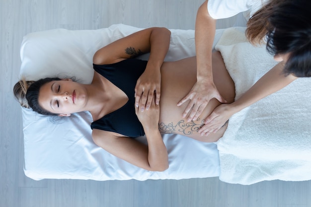 Foto colpo di bella giovane donna fisioterapista che massaggia la pancia della donna incinta su una barella a casa.