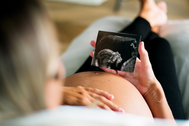 Photo shot of beautiful young pregnant woman looking ultrasound of her baby while resting on the sofa