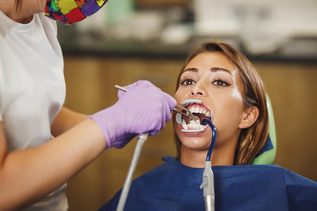 Shot of a beautiful young woman is at the dentist. She sits in the dentist's chair and the dentist preparing to sets braces on her teeth putting aesthetic self-aligning lingual locks.