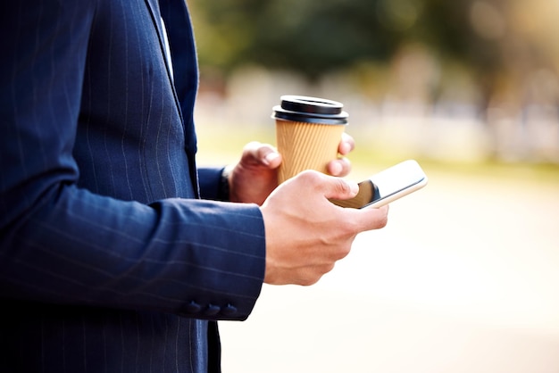 Shot of a businessman using his smartphone while drinking coffee