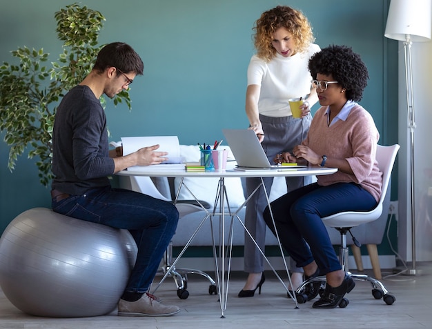 Photo shot of casual young business people working with laptop and talking of they new project together in the office.