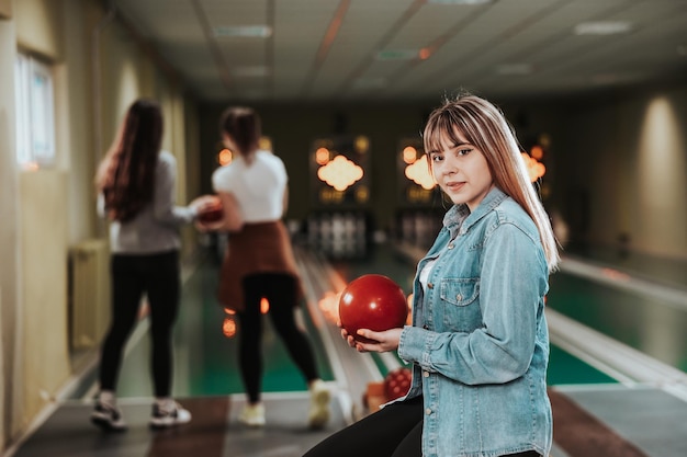 Photo shot of a cute young woman holding bowling ball at the bowling club and looking at camera.