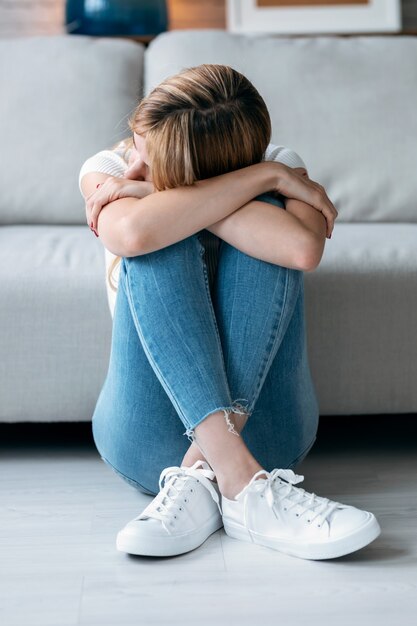 Photo shot of depresive young woman thinking about her problems while sitting on the floor in the living room at home.