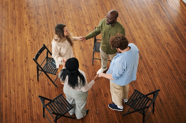 Above shot of four interracial people holding by hands while standing in circle