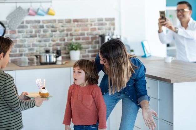 彼の兄弟が家でそれを持っている間、彼の誕生日ケーキのろうそくを吹き消す面白い男の子のショット。