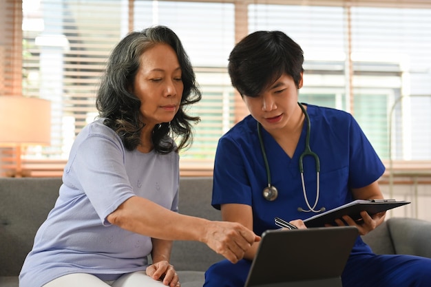 高齢の女性患者に健康検査の実験結果を共有するラップトップの画面を指さしている一般医の男性のショット
