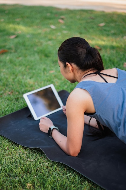 태블릿 컴퓨터에서 튜토리얼 비디오를 시청하는 동안 공원에서 운동하는 소녀의 샷