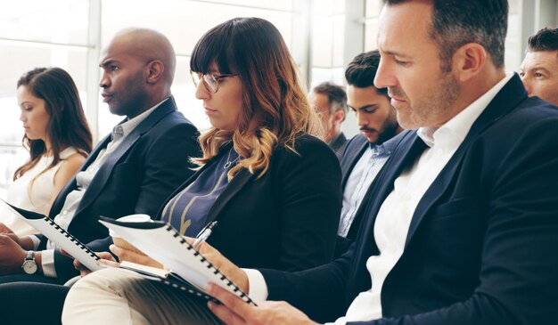 Shot of a group of businesspeople taking down notes while attending a conference