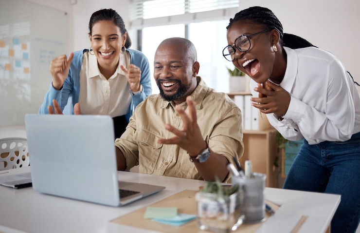Photo shot of a group of businesspeople using a laptop and cheering in a modern office
