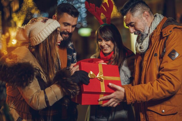 Shot of a group of cheerful young friends with Xmas gifts having fun at a night out.