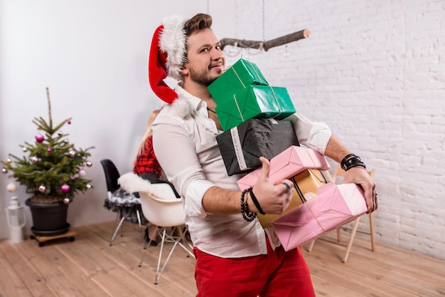 Снимок счастливых друзей, наслаждающихся праздником, фокусируется на мужчине с подарочными коробками на переднем плане в ...