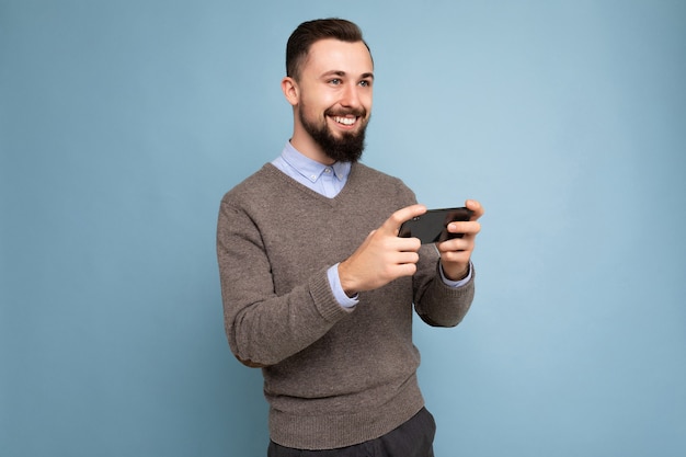 Shot of happy handsome young brunette unshaven man with beard wearing everyday grey sweater and blue shirt