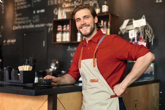 Shot of happy young bar owner standing near the counter and looking away smiling