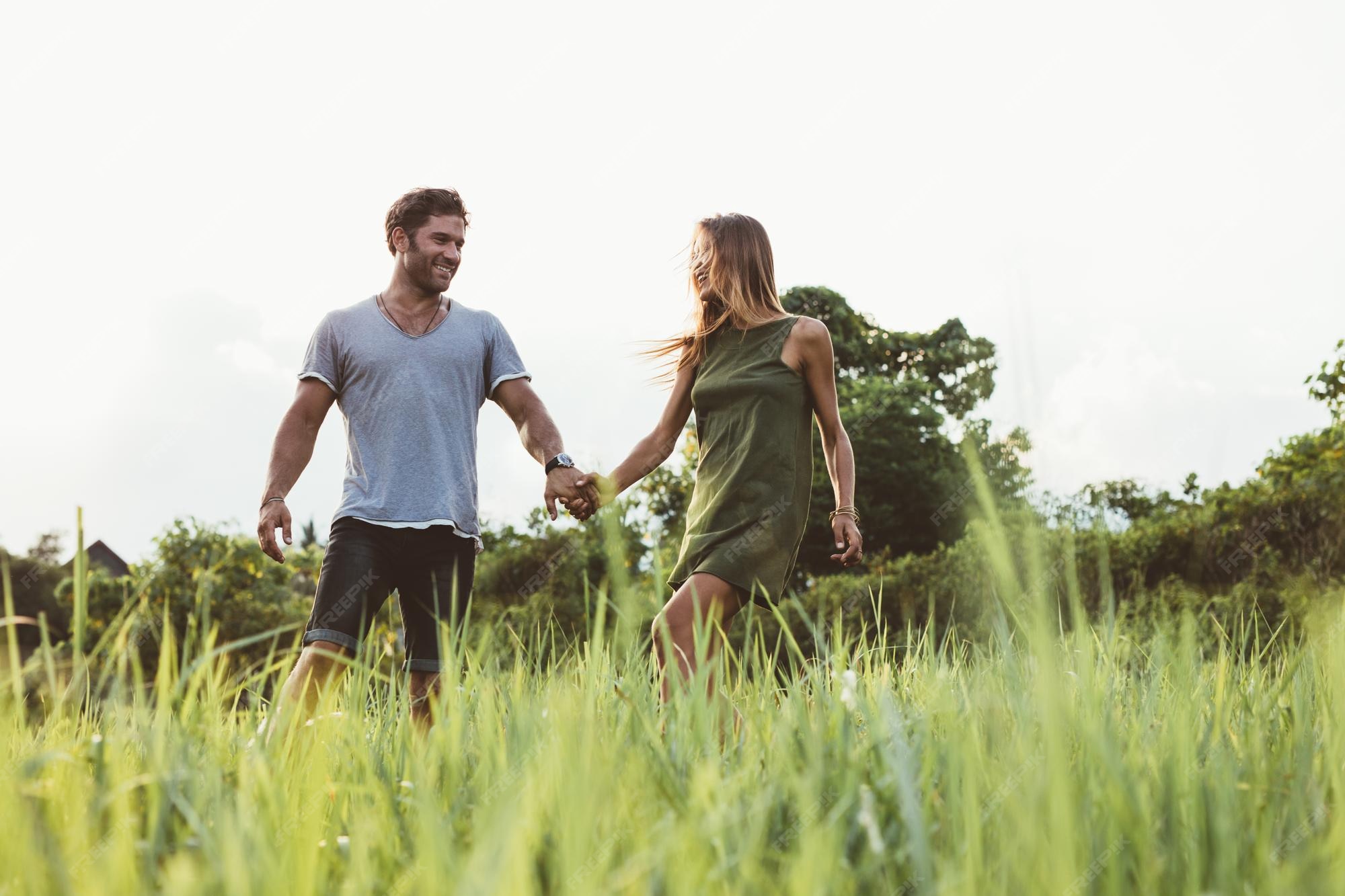 Premium Photo | Shot of happy young couple walking in the meadow man and woman holding hands and walking together in field of tall grass