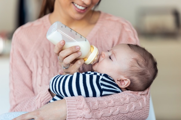 幸せな若い母親が自宅で哺乳瓶で赤ちゃんの息子を養っているショット。