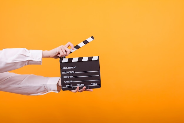 Shot of isolated hands on yellow background holding a clapper. Teenage girl holding clapper in studio.