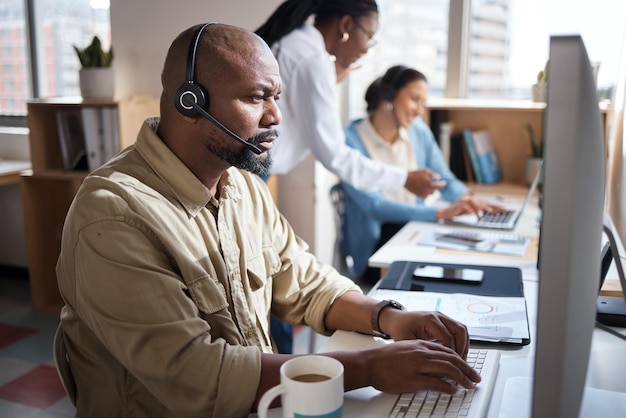 Shot of a mature businessman using a headset in a modern office with his colleagues working in the background