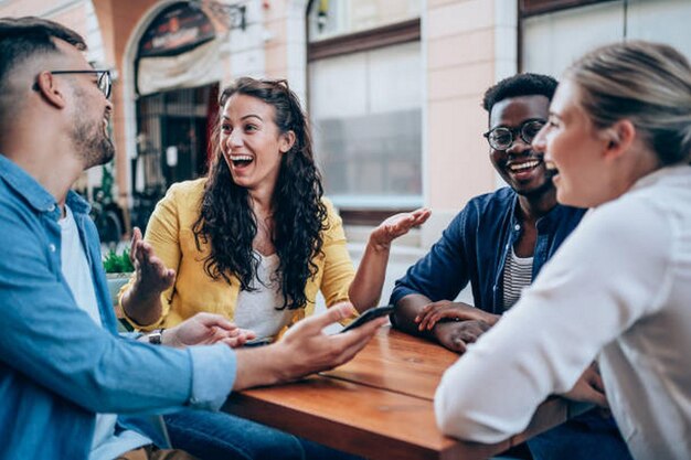 shot of multiracial group of young people sitting in a sidewalk cafe talking drinking coffee smilin
