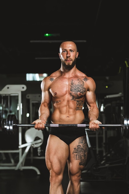 Photo shot of a muscular bodybuilder doing hard training with barbell for his arms muscles at the gym.