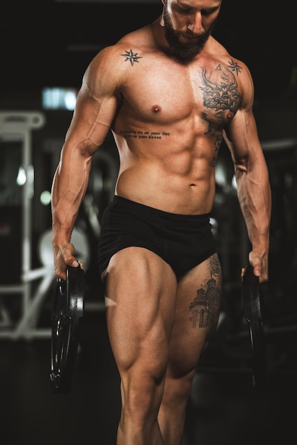Снимок мускулистого бодибилдера, показывающего свои идеальные мышцы после тренировки с весовой платформой в тренажерном зале.