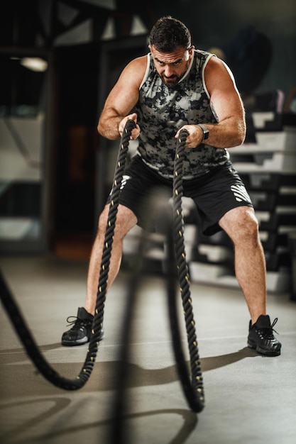 ジムでロープを使ってエクササイズをしているスポーツウェアの筋肉質の男のショット。