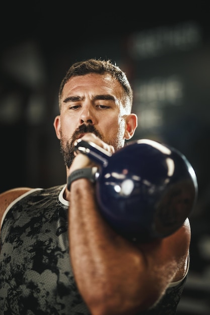 Снимок мускулистого парня в спортивной одежде, выполняющего упражнения на пресс с гирями в спортзале.