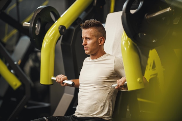 Снимок мускулистого парня в спортивной одежде, работающего в тренажерном зале. Он накачивает грудную мышцу тяжелым весом.