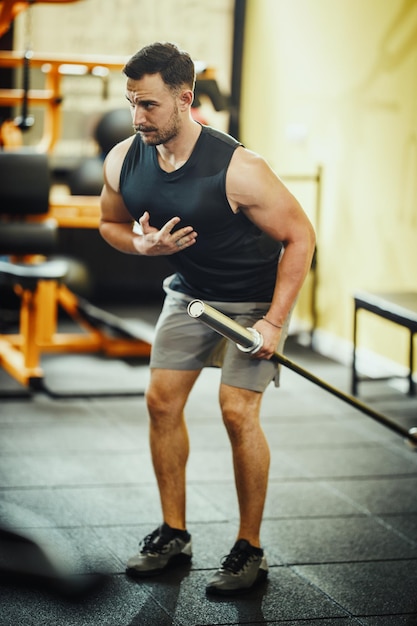 Shot of a muscular guy in sportswear working out with barbell at the cross training gym.