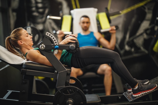 Inquadratura di una giovane donna muscolosa in abiti sportivi che si allena in palestra. sta facendo esercizi per il ponte del gluteo per i suoi glutei sulla macchina per l'anca.