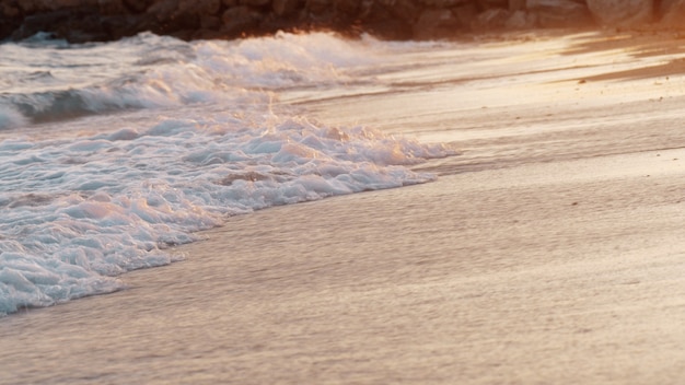 Фото Кадр пенистых волн, омывающих морской берег в теплом свете заката
