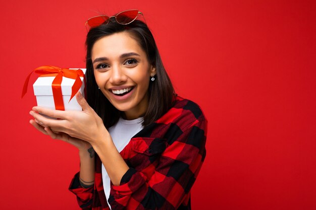Shot of  positive smiling young  woman isolated over red background wall wearing white