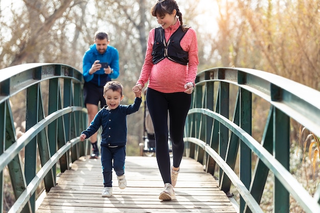 Shot of pregnant young woman with her little son enjoying the time together outdoor while her husband take a photographs.