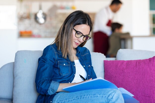 自宅のソファに座って仕事のメモを書いているきれいな女性のショット。