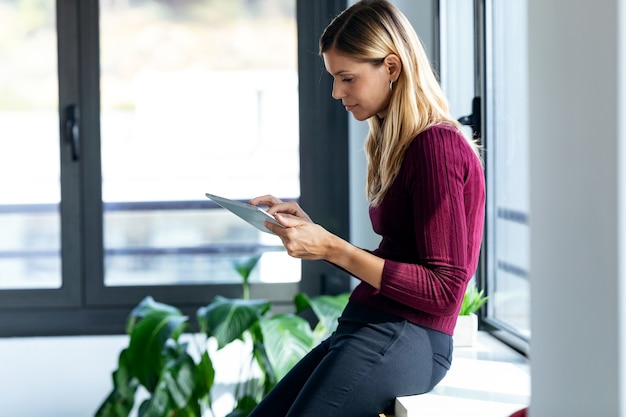 Shot of pretty young business woman using her digital tablet while sitting next to the window in the office.