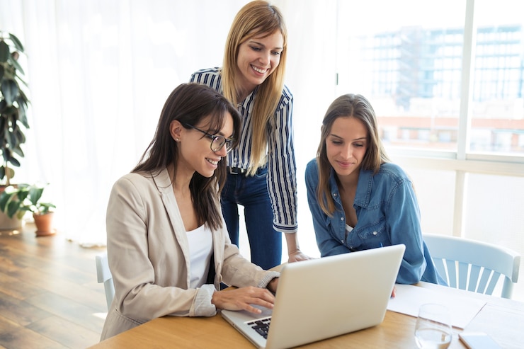 Photo shot of pretty young businesswoman showing progress of work on laptop to co-workers in the office.
