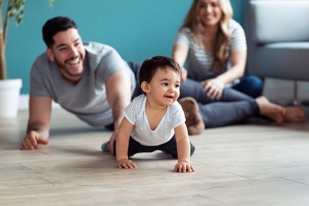Снимок довольно молодых родителей, играющих с маленьким сыном, сидя на полу дома.