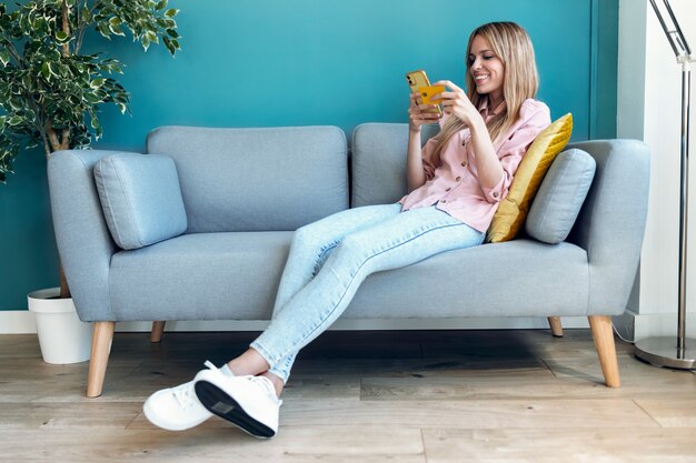 Shot of pretty young woman shopping online with credit card and smartphone while sitting on sofa at home.