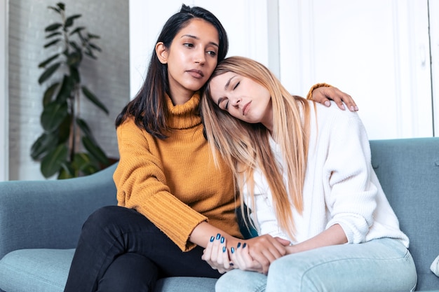 Shot of pretty young woman supporting and comforting her sad friend while sitting on the sofa at home.