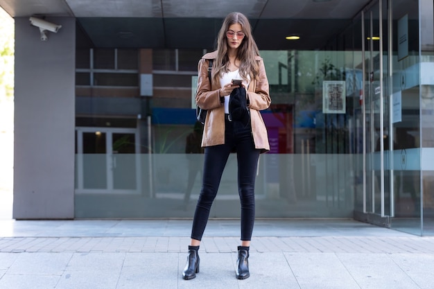 Shot of pretty young woman using her mobile phone while standing in the street.