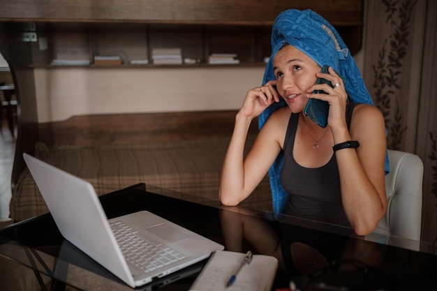 Shot of pretty young woman using her mobile phone while working with laptop sitting at home