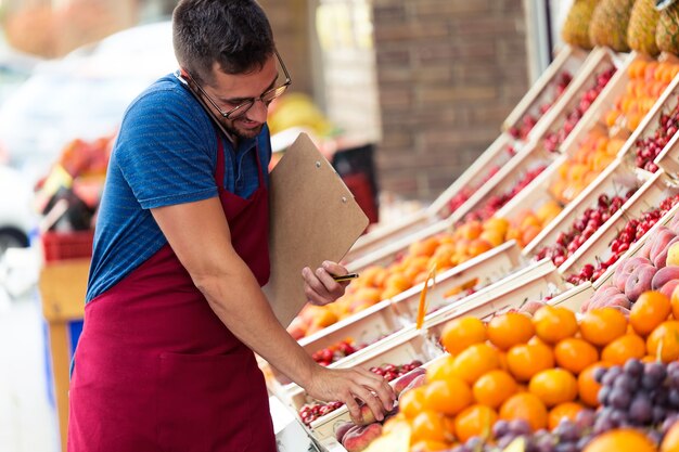 Shot of salesman selecting fresh fruit and talking on the phone in health grocery shop.